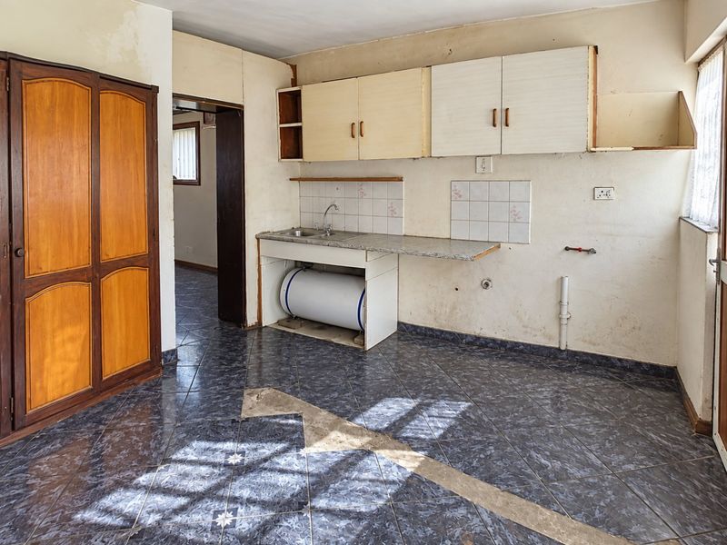A dated kitchen area featuring basic cabinetry, a sink, and tiled flooring, requiring significant renovation and cosmetic updates to modernize the space.