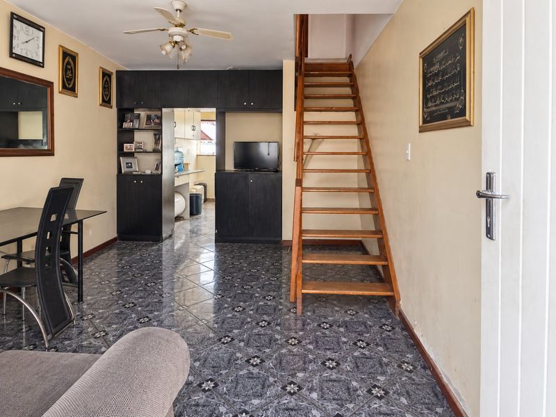 Open plan living area featuring tiled flooring, built-in storage cabinetry, and a wooden staircase leading to the upper level.
