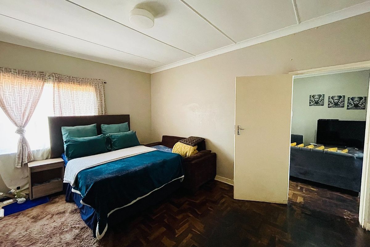 A bedroom featuring traditional parquet flooring and neutral wall tones, offering a functional space with direct access to an adjacent living area.