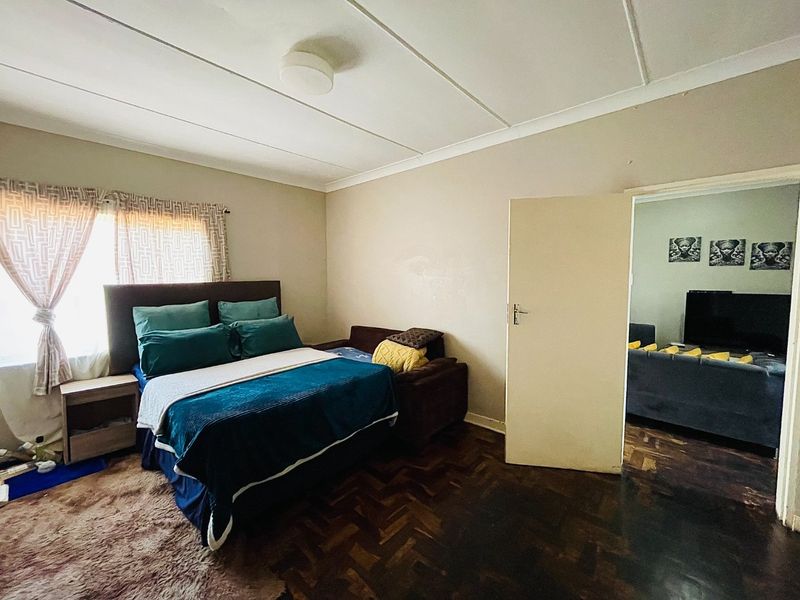 A bedroom featuring traditional parquet flooring and neutral wall tones, offering a functional space with direct access to an adjacent living area.