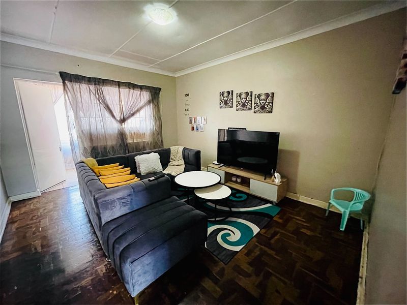 A living room featuring traditional parquet flooring and ceiling cornice detail, offering a functional space with potential for cosmetic updates.