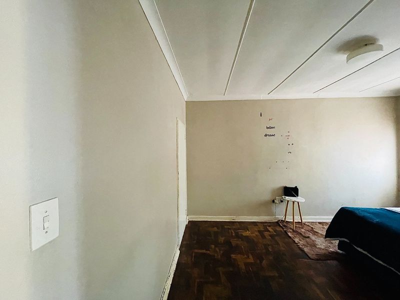 A bedroom featuring traditional parquet flooring, neutral wall tones, and a simple ceiling light fixture, offering a blank canvas for personalization.