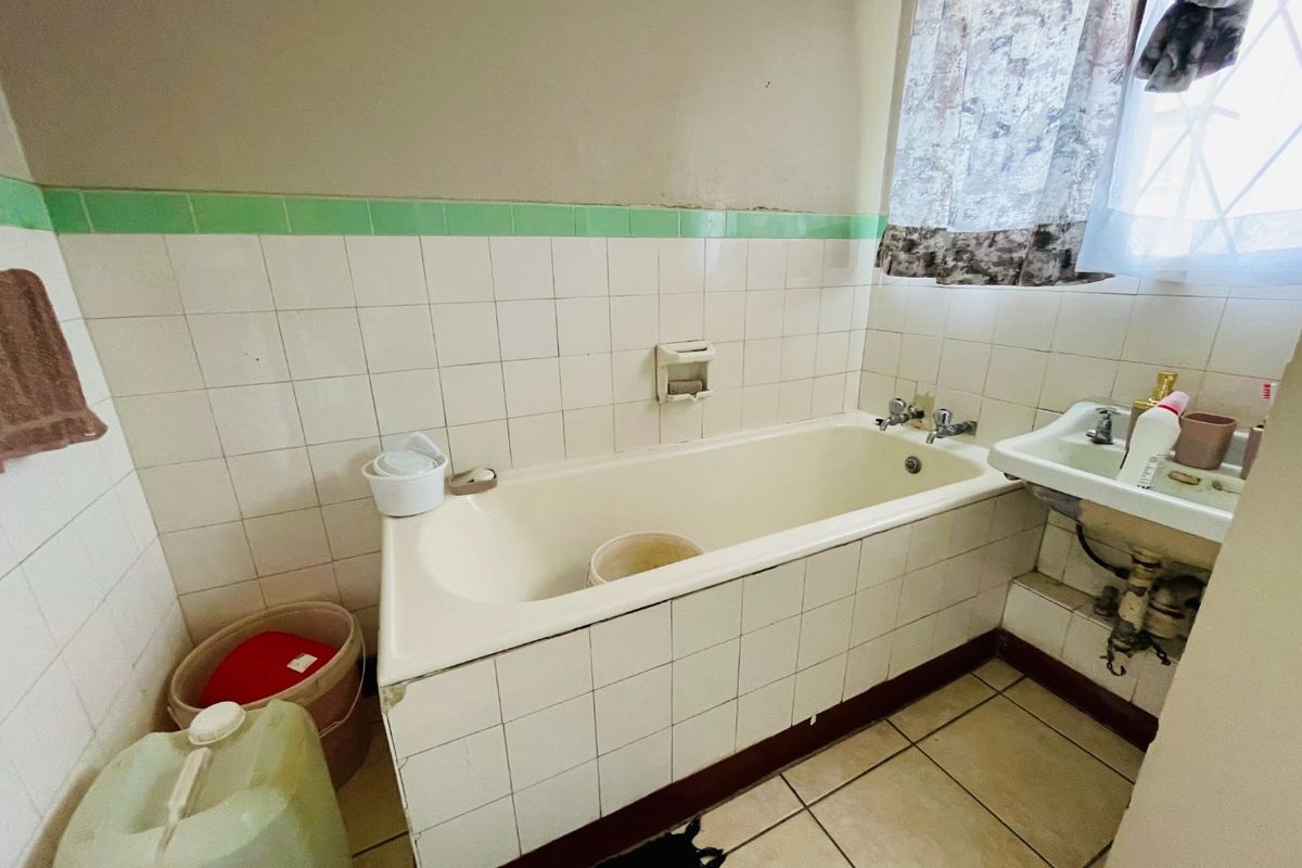 A dated bathroom featuring a tiled bathtub, wall-mounted basin, and ceramic tiling throughout, requiring modernization to improve its overall condition and aesthetic appeal.