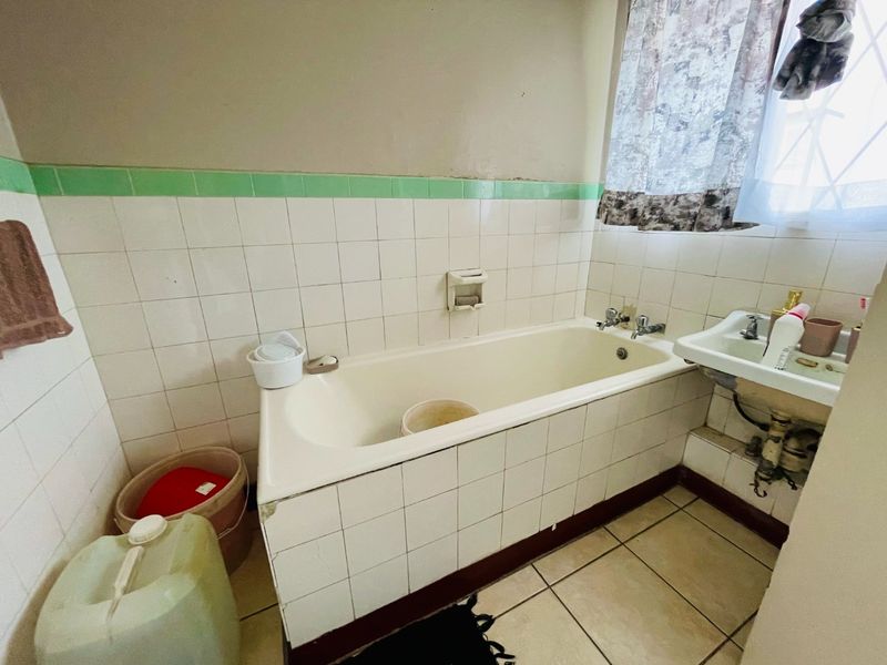 A dated bathroom featuring a tiled bathtub, wall-mounted basin, and ceramic tiling throughout, requiring modernization to improve its overall condition and aesthetic appeal.
