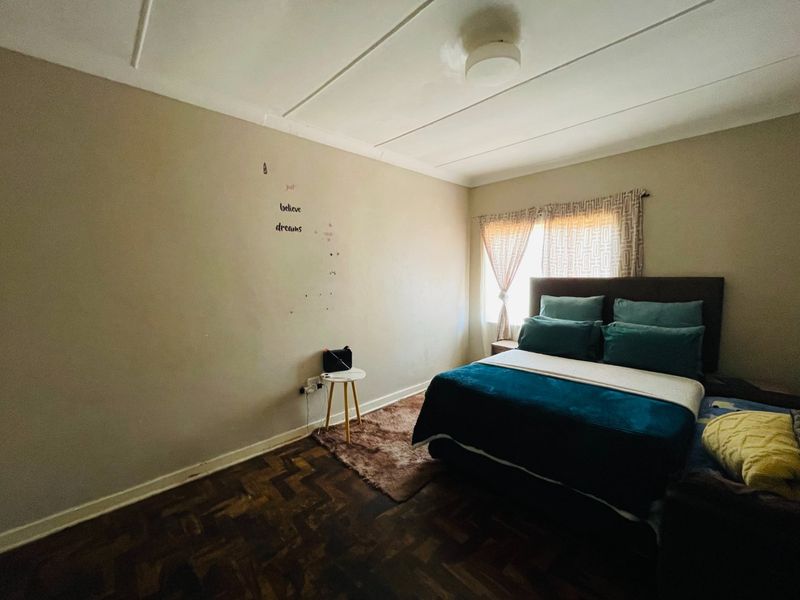 A bedroom featuring traditional parquet flooring and a tiled ceiling, offering a functional space with potential for cosmetic updates.