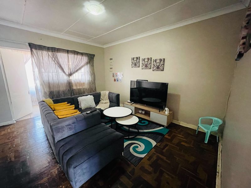 A living room featuring traditional parquet flooring and coved ceilings, offering a functional space with direct access to an adjacent area.