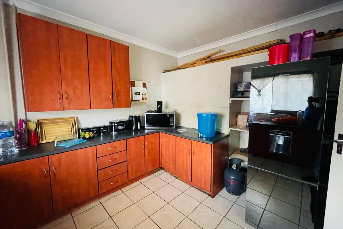 A functional kitchen featuring wood-look cabinetry, dark countertops, and tiled flooring, offering potential for modernization and improved storage organization.