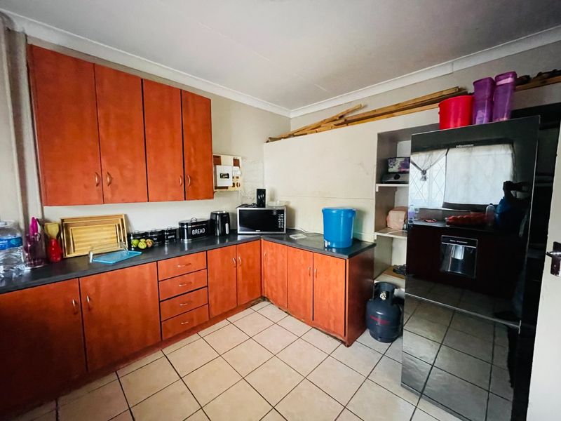 A functional kitchen featuring wood-look cabinetry, dark countertops, and tiled flooring, offering potential for modernization and improved storage organization.