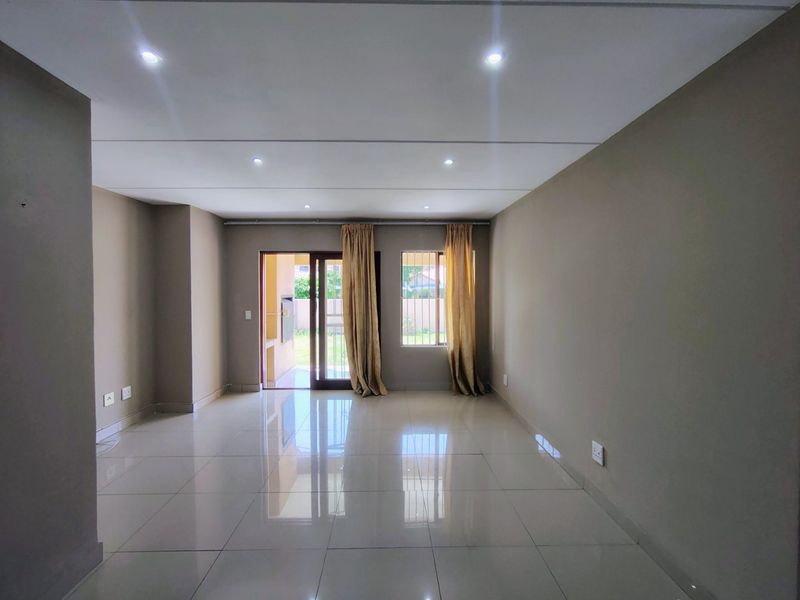 A spacious, empty living room featuring neutral tiled flooring, recessed downlighting, and direct access to an outdoor patio area through a sliding glass door.