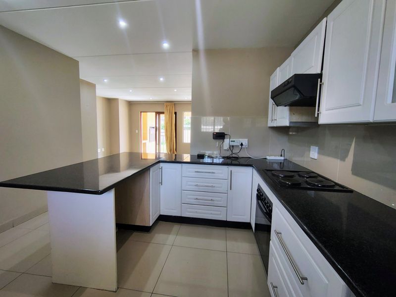 Modern open-plan kitchen featuring granite countertops, white cabinetry, built-in oven and hob, and tiled flooring, flowing into an adjacent living area.