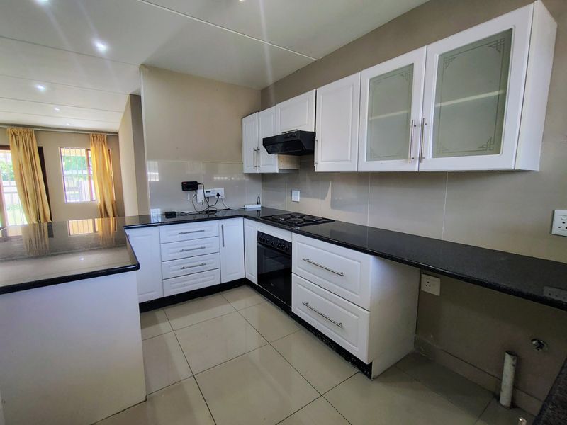 Modern kitchen featuring granite countertops, built-in oven, gas hob, extractor fan, and ample white cabinetry with glass-fronted display units.