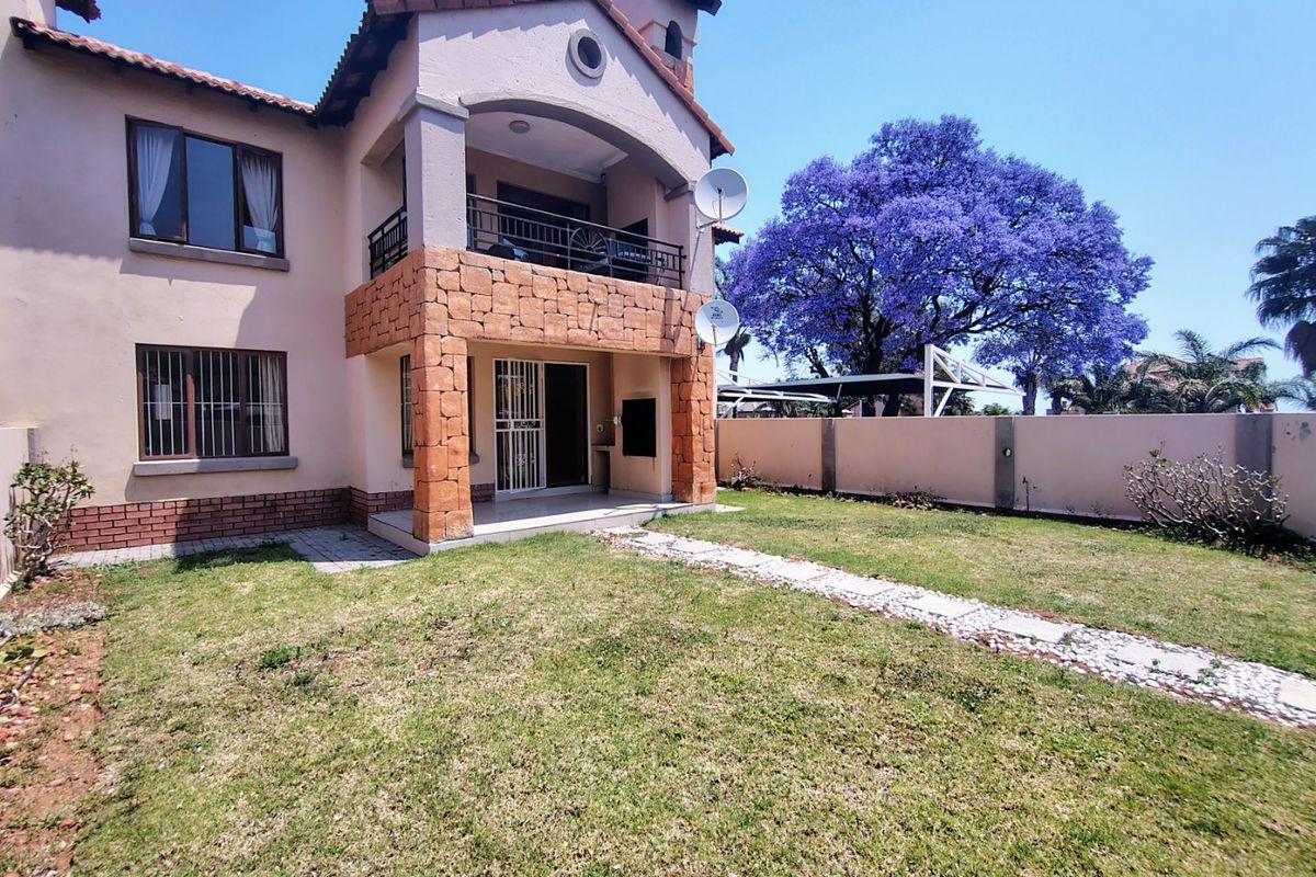 Rear view of the apartment featuring a stone-clad balcony, security gate, and a private garden area with a paved walkway.