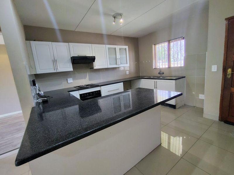 A clean, functional kitchen featuring granite countertops, built-in cabinetry, an electric hob with extractor, and tiled flooring throughout.