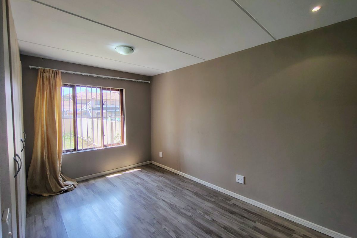 A bright, empty bedroom featuring modern laminate flooring, built-in cupboards, and security bars on the window.