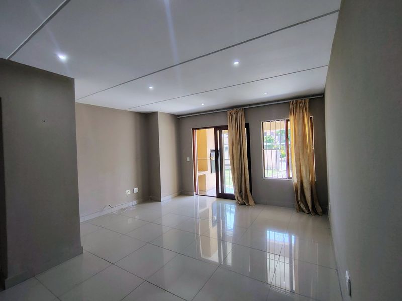 A spacious, empty living room featuring neutral walls, polished tiled flooring, recessed lighting, and a sliding glass door providing access to the exterior.