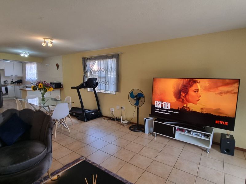 Open-plan living and dining area featuring tiled flooring, security bars on windows, and an adjoining kitchen with built-in cabinetry and appliances.