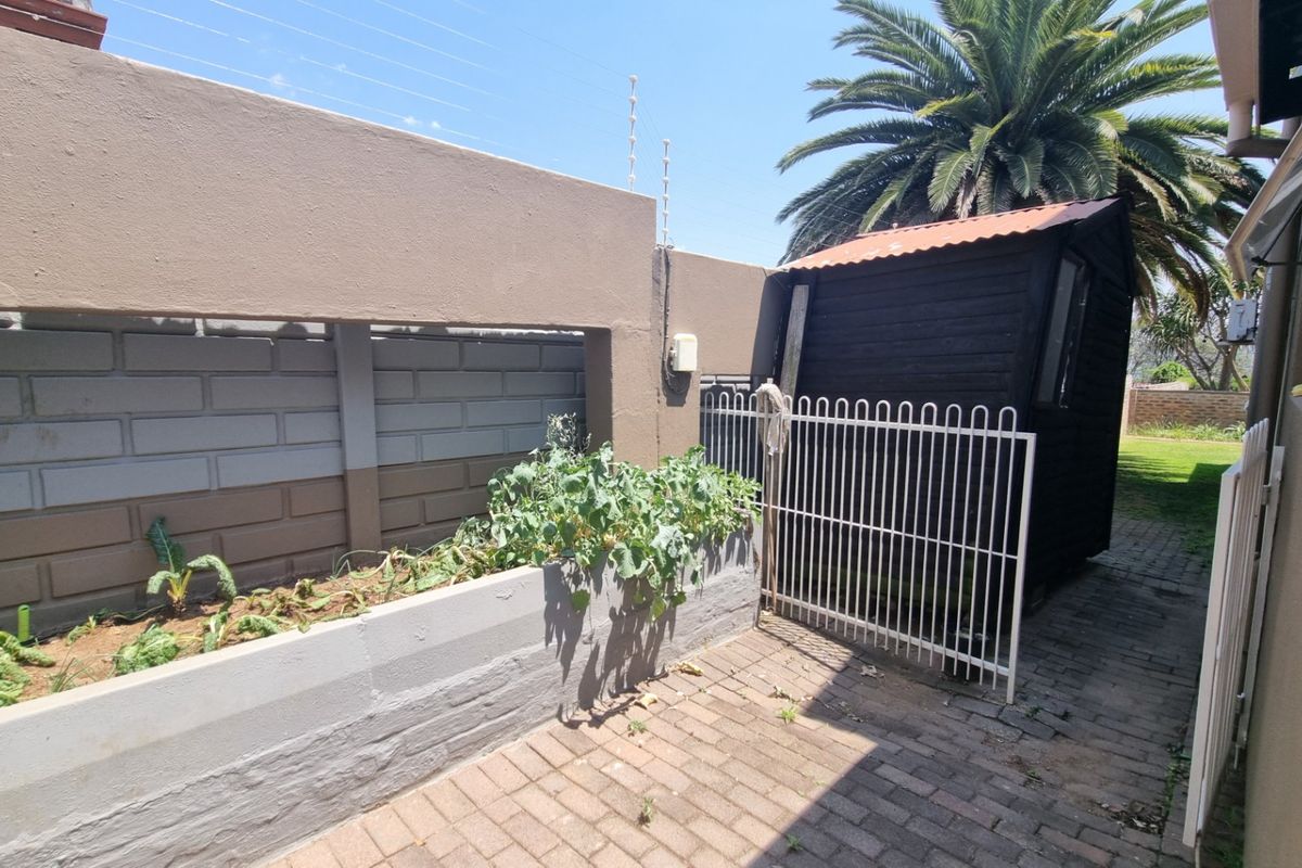 Rear courtyard area featuring brick paving, a raised garden bed, perimeter wall with electric fencing, and a detached wooden storage shed.
