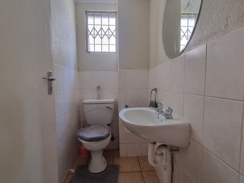 A compact guest bathroom featuring a pedestal basin, toilet, and tiled finishes, requiring minor repairs to the door frame area.