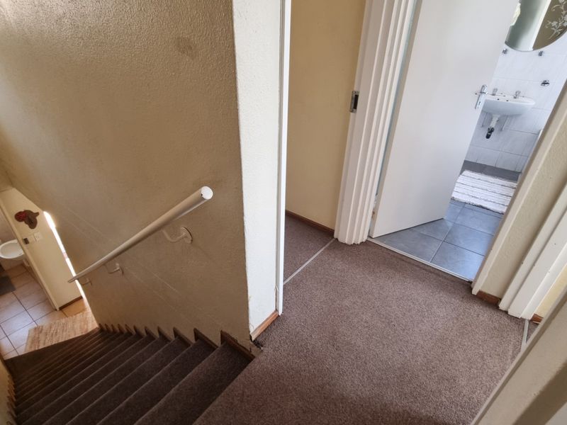 A view from the top of a carpeted staircase looking down towards a lower level and into an adjacent bathroom.