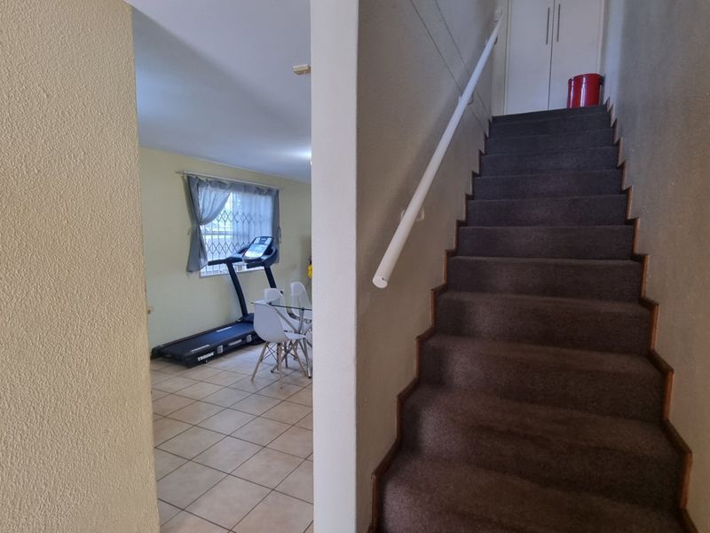 A view from the hallway showing a carpeted staircase with a handrail, leading towards an adjacent living area with tiled flooring.