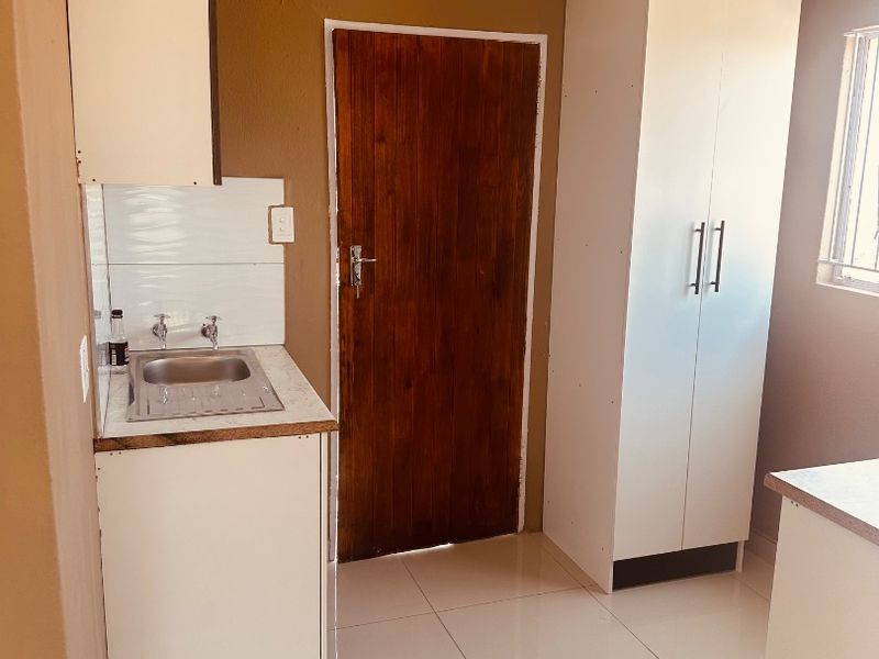 A compact kitchen area featuring tiled flooring, built-in cabinetry with a stainless steel sink, and a timber door, offering a functional space for updates.
