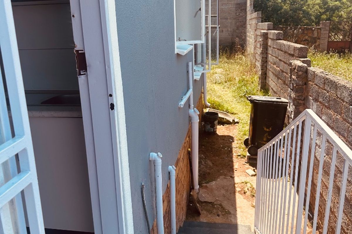 Rear exterior view showing a concrete staircase with metal handrails, external plumbing, and a brick boundary wall along the side of the house.