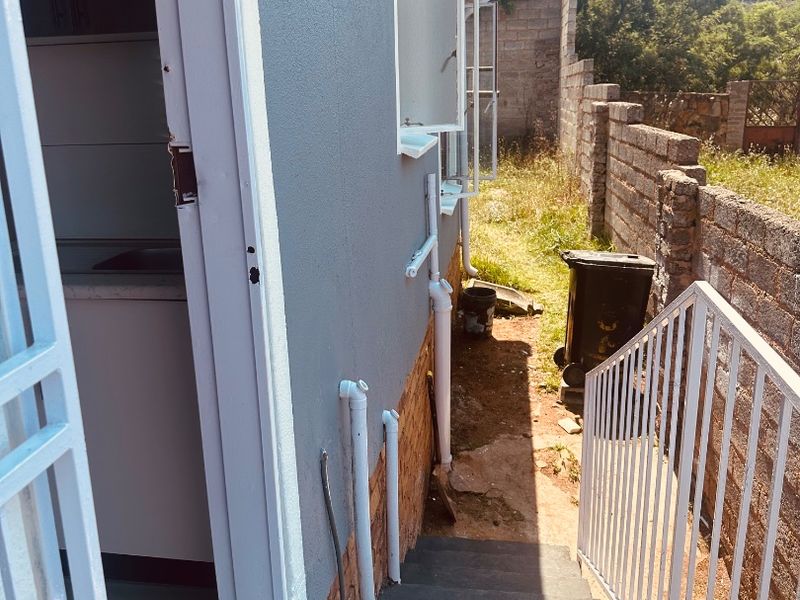 Rear exterior view showing a concrete staircase with metal handrails, external plumbing, and a brick boundary wall along the side of the house.