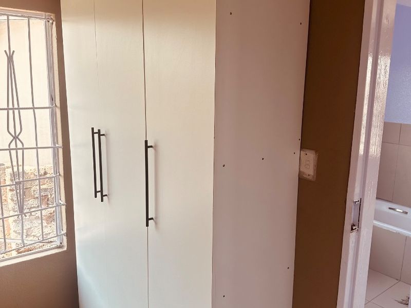A bedroom featuring a white built-in wardrobe with modern handles, tiled flooring, and a window fitted with security bars.