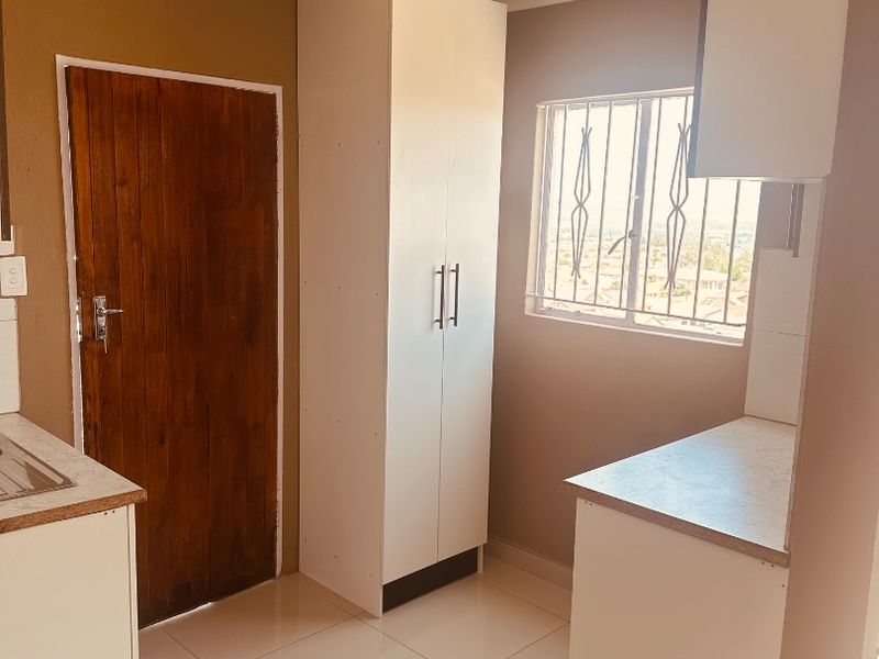 A compact kitchen featuring white built-in cabinetry, tiled flooring, and a window with security bars, offering a functional and clean preparation space.