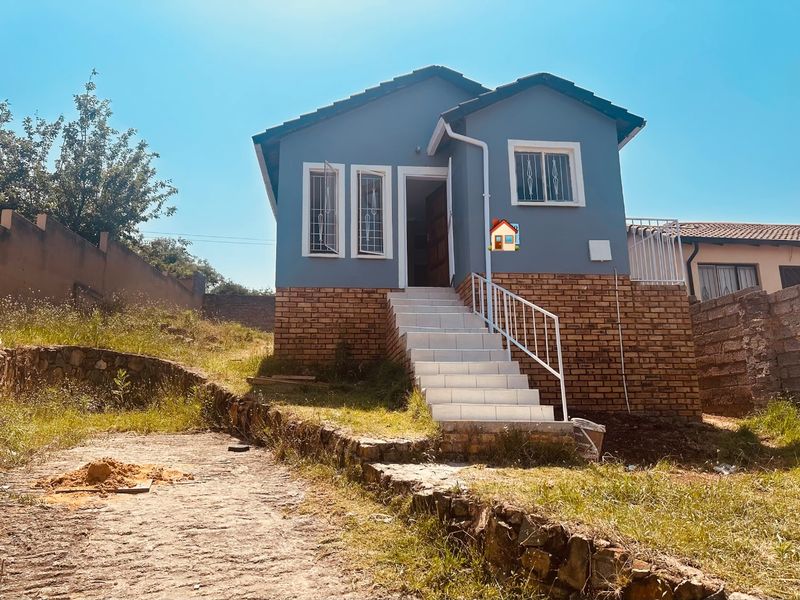 Front elevation of a detached house featuring a brick base, tiled entrance staircase with security railings, and window security bars.