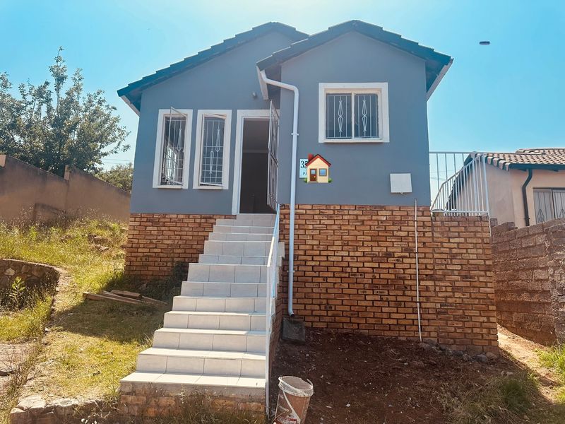 Front elevation of a detached house featuring a tiled staircase entrance, brick base, and grey painted upper walls with security bars on windows.
