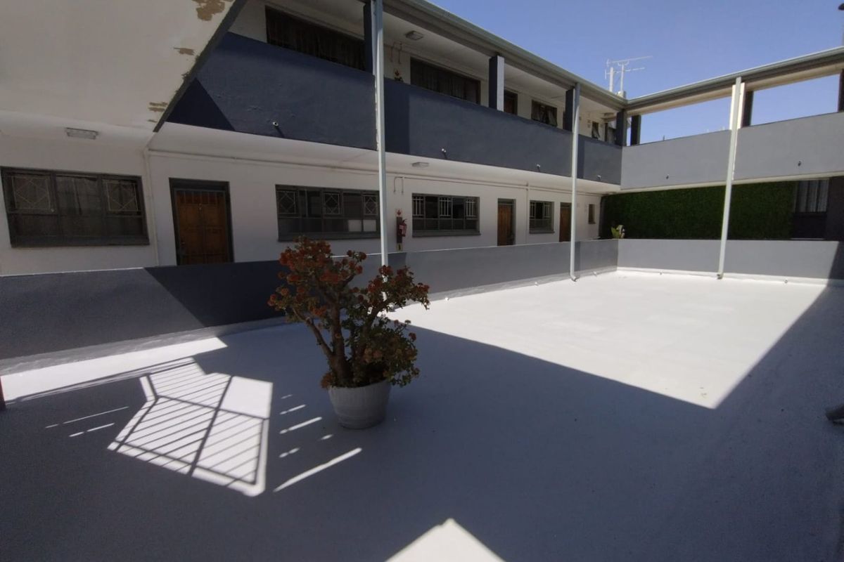 An open-air communal balcony area in an apartment complex featuring painted concrete flooring and metal structural supports.