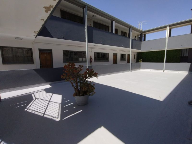 An open-air communal balcony area in an apartment complex featuring painted concrete flooring and metal structural supports.