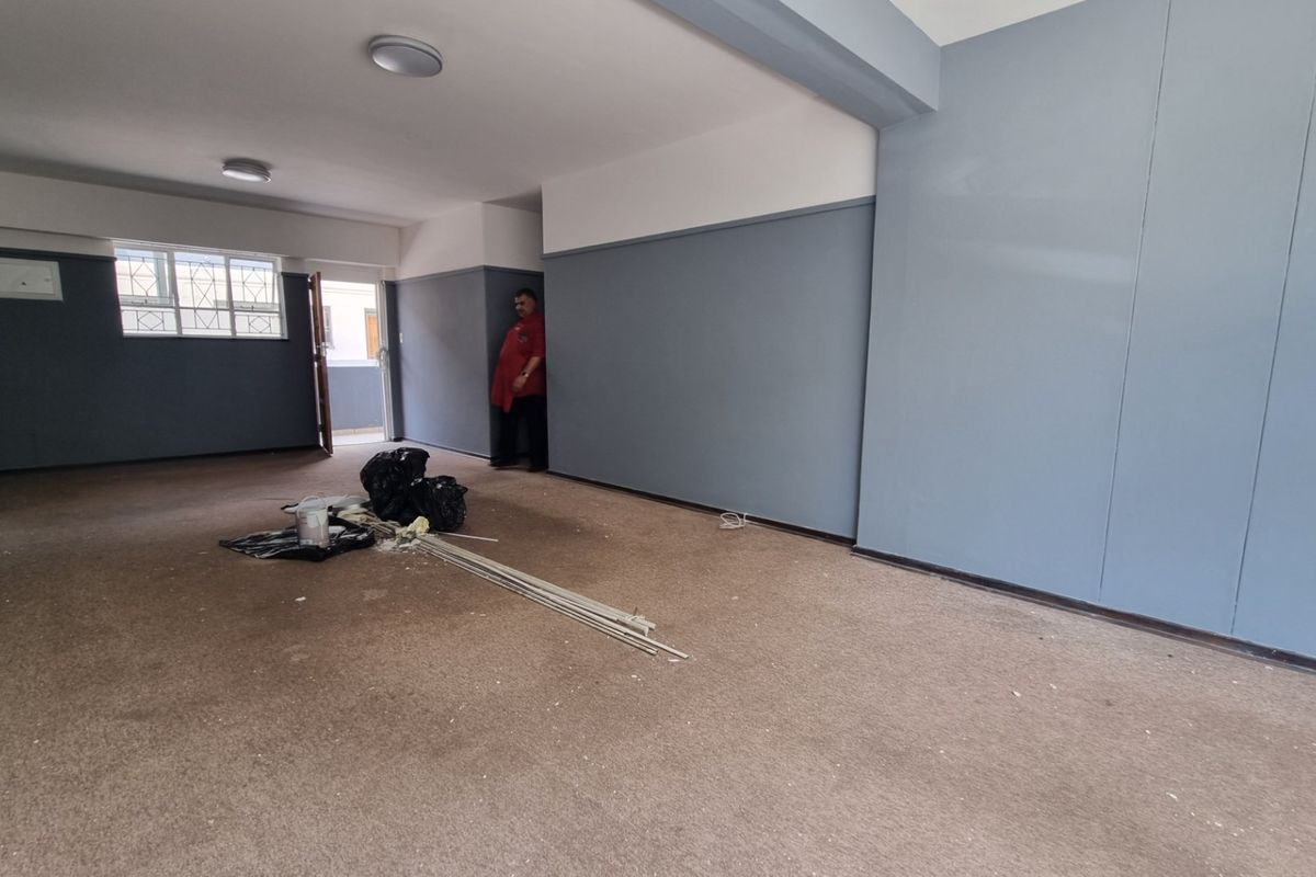 An empty, open-plan living area featuring neutral grey walls, carpeted flooring, and natural light from an adjacent balcony entrance.