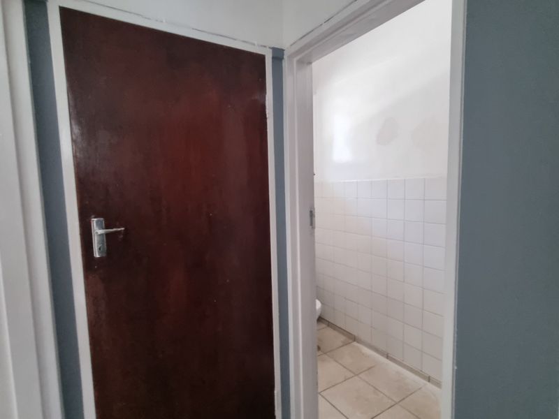 A functional hallway area featuring tiled flooring and access to adjacent rooms, showing signs of wear and requiring cosmetic updates.
