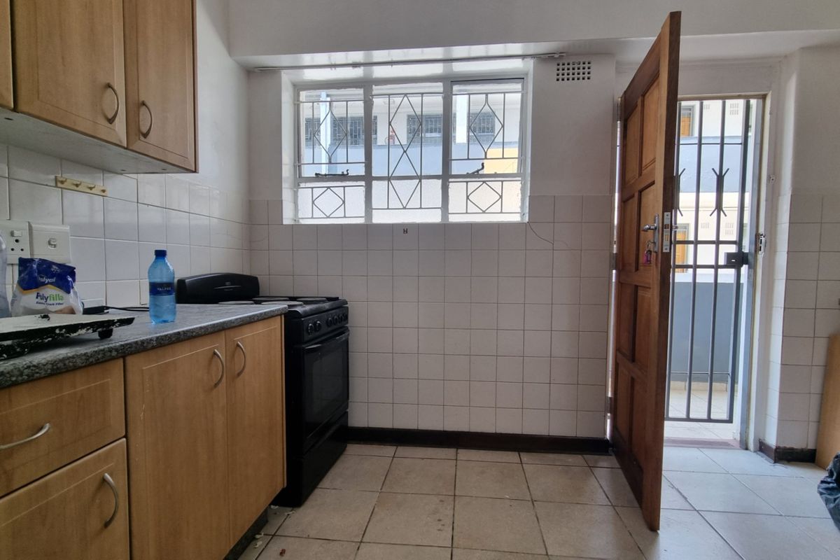 A functional kitchen featuring laminate cabinetry, tiled splashbacks, and a freestanding stove, with direct access to an exterior area through a security door.