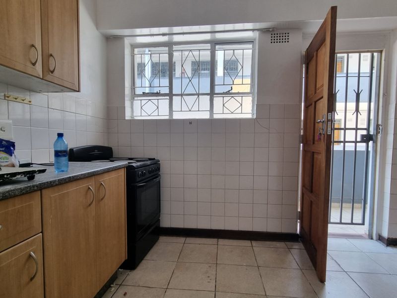 A functional kitchen featuring laminate cabinetry, tiled splashbacks, and a freestanding stove, with direct access to an exterior area through a security door.