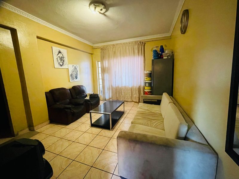 A living room featuring tiled flooring and ceiling cornicing, currently requiring cosmetic updates to modernize the space.