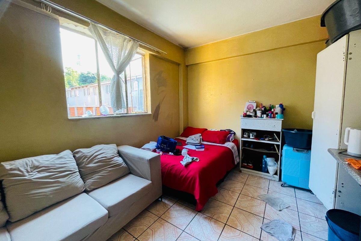 A compact bedroom featuring tiled flooring and a large window, currently requiring cosmetic updates and wall repairs to improve the overall living space.