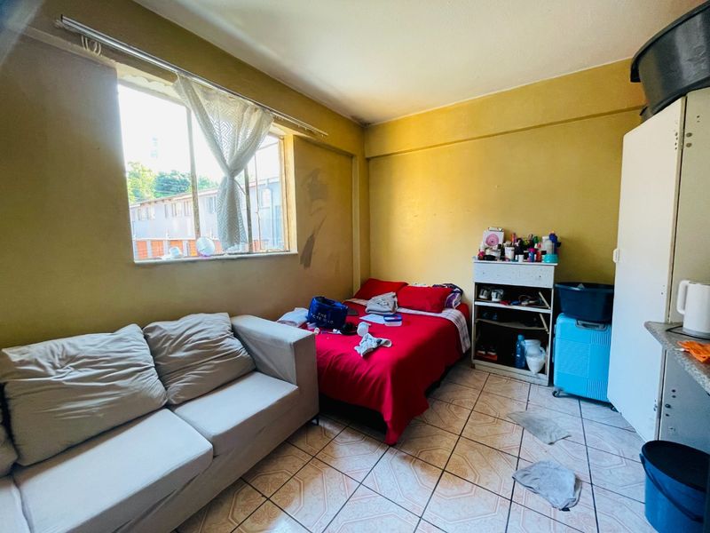 A compact bedroom featuring tiled flooring and a large window, currently requiring cosmetic updates and wall repairs to improve the overall living space.