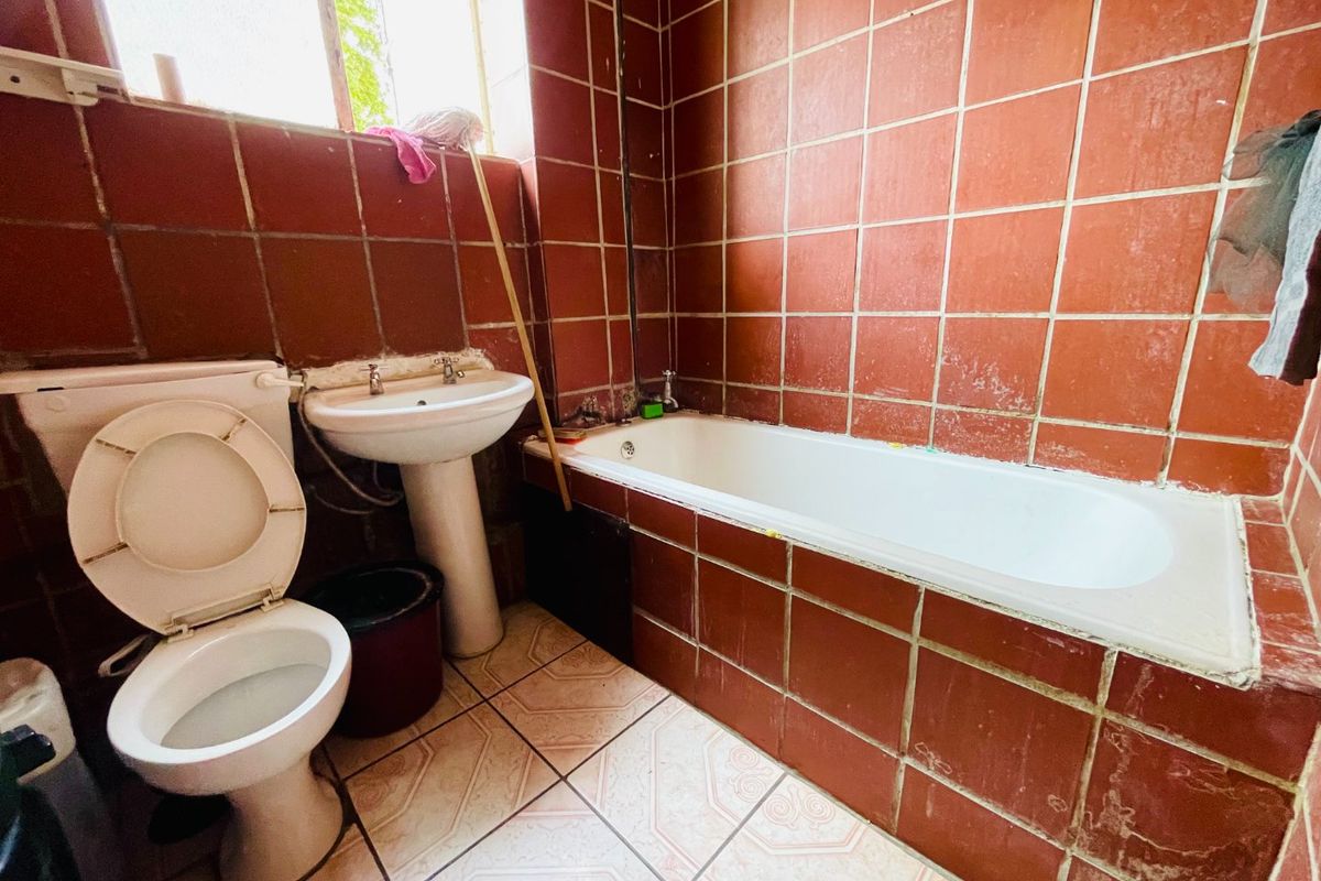 A dated bathroom featuring a pedestal basin, built-in bathtub, and terracotta-style wall tiling, requiring cosmetic updates and maintenance to improve its overall condition.