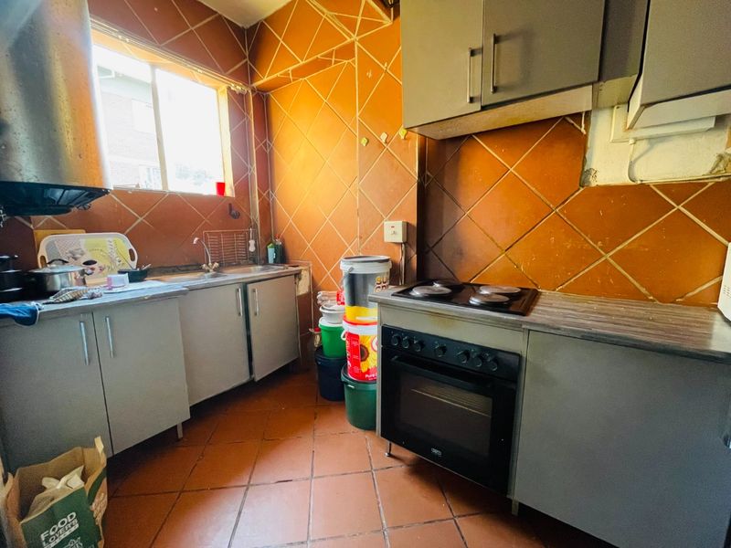A compact kitchen featuring built-in cabinetry, a stainless steel sink, and an integrated electric stove and oven with tiled finishes throughout.
