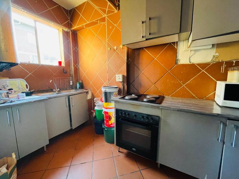 A dated kitchen featuring built-in cabinetry, an electric oven and hob, and tiled finishes throughout, requiring cosmetic updates to modernize the space.