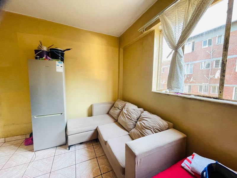 A living area featuring tiled flooring and a large window, providing natural light. The space requires cosmetic updates to improve its overall condition.
