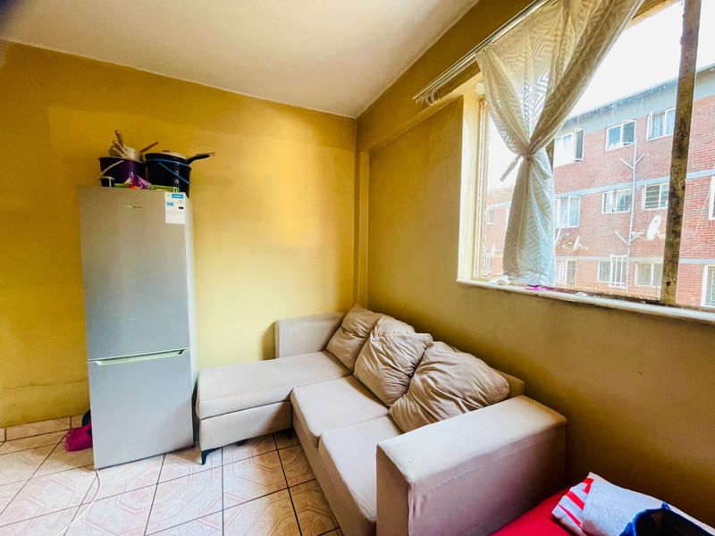 A compact living area featuring tiled flooring and a large window, currently requiring cosmetic updates to the wall finishes.