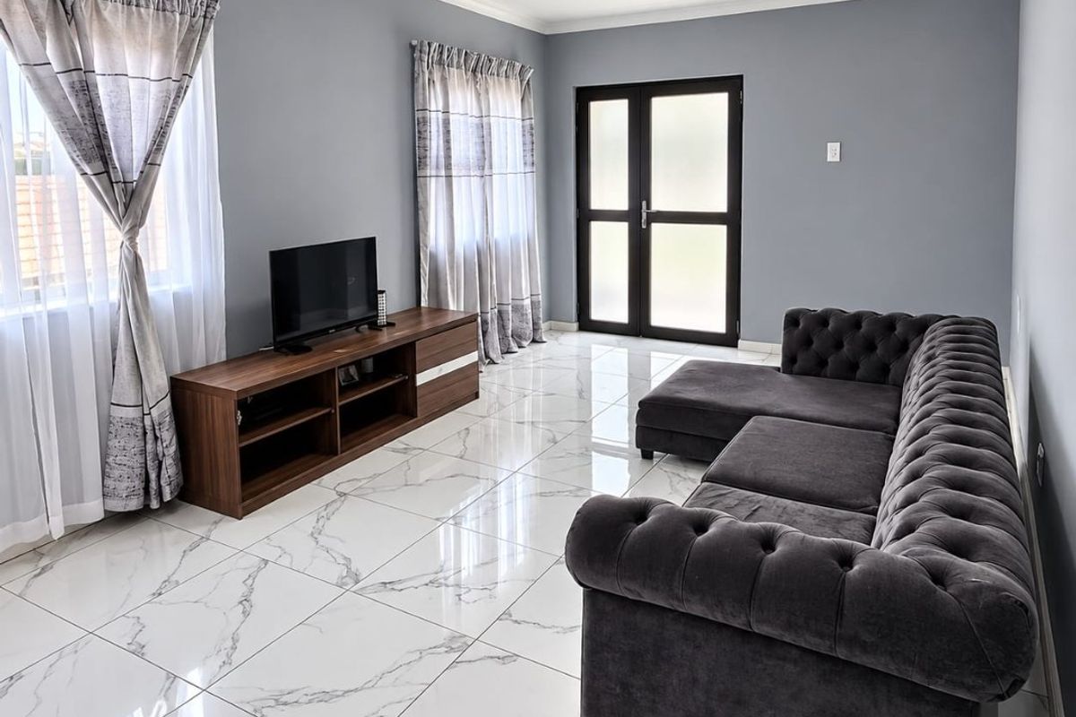 A modern living room featuring polished marble-look floor tiles, neutral grey walls, and double glass-panelled doors providing natural light.