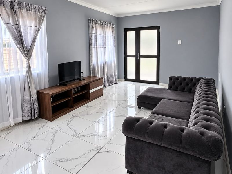 A modern living room featuring polished marble-look floor tiles, neutral grey walls, and double glass-panelled doors providing natural light.