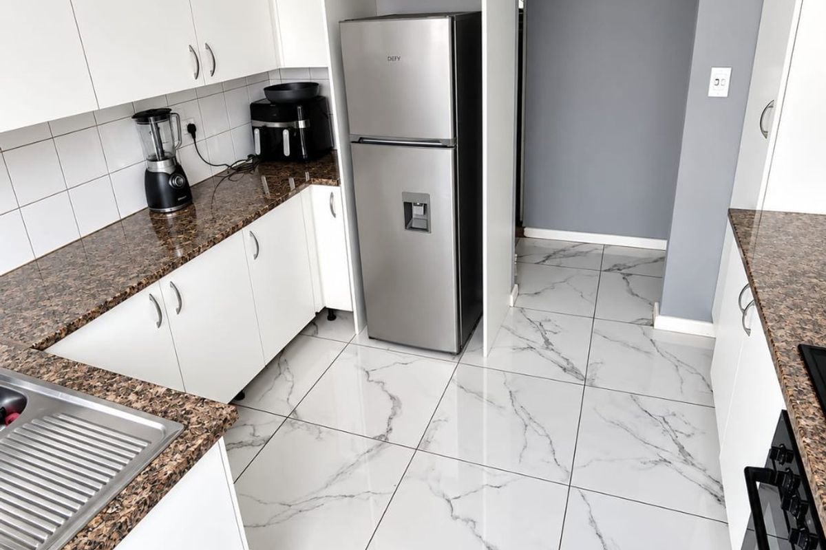 Modern kitchen featuring white cabinetry, granite countertops, marble-look floor tiles, and integrated stainless steel appliances.