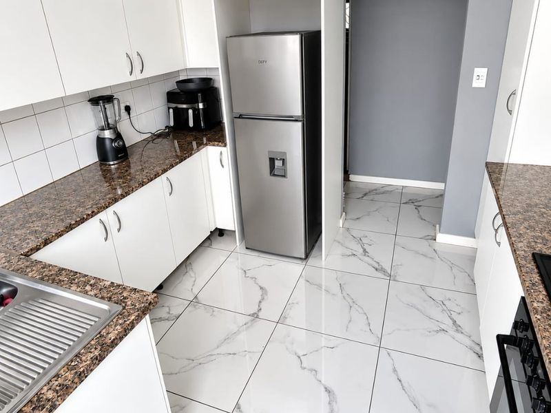 Modern kitchen featuring white cabinetry, granite countertops, marble-look floor tiles, and integrated stainless steel appliances.