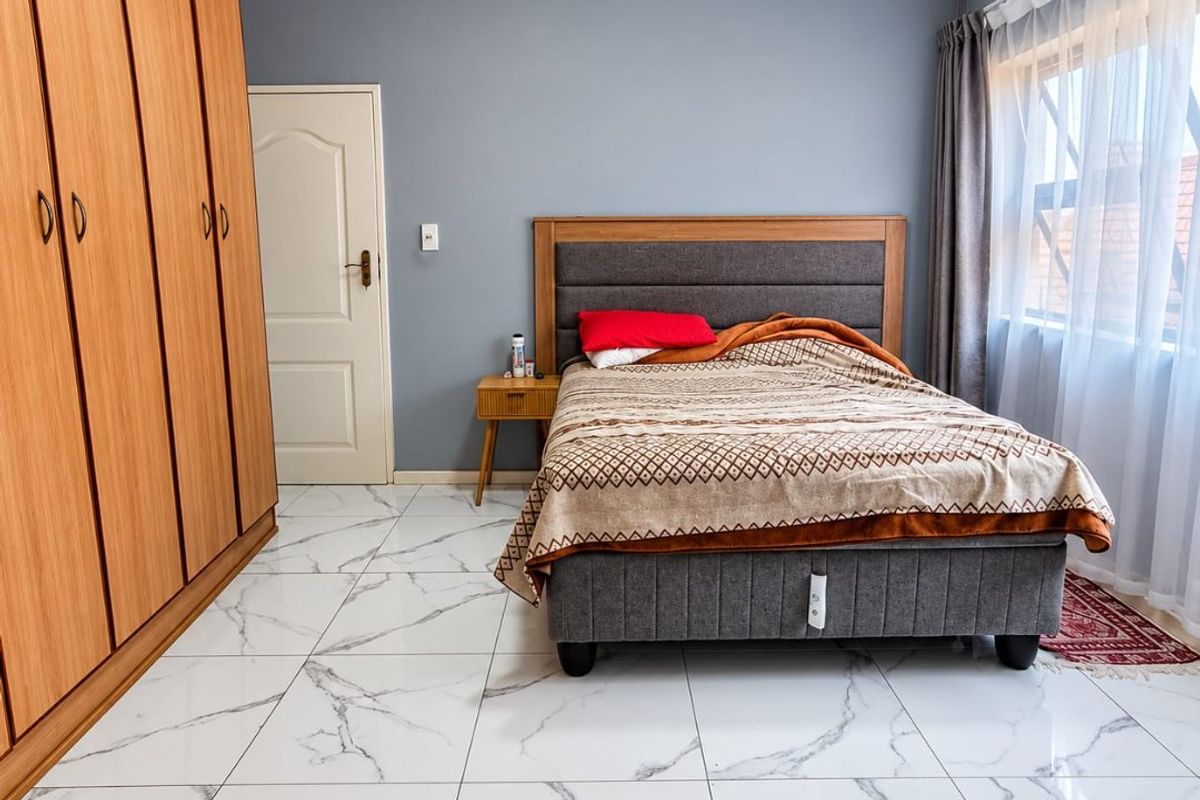 A well-maintained bedroom featuring modern marble-look floor tiles, a large built-in wooden wardrobe, and neutral grey wall finishes.